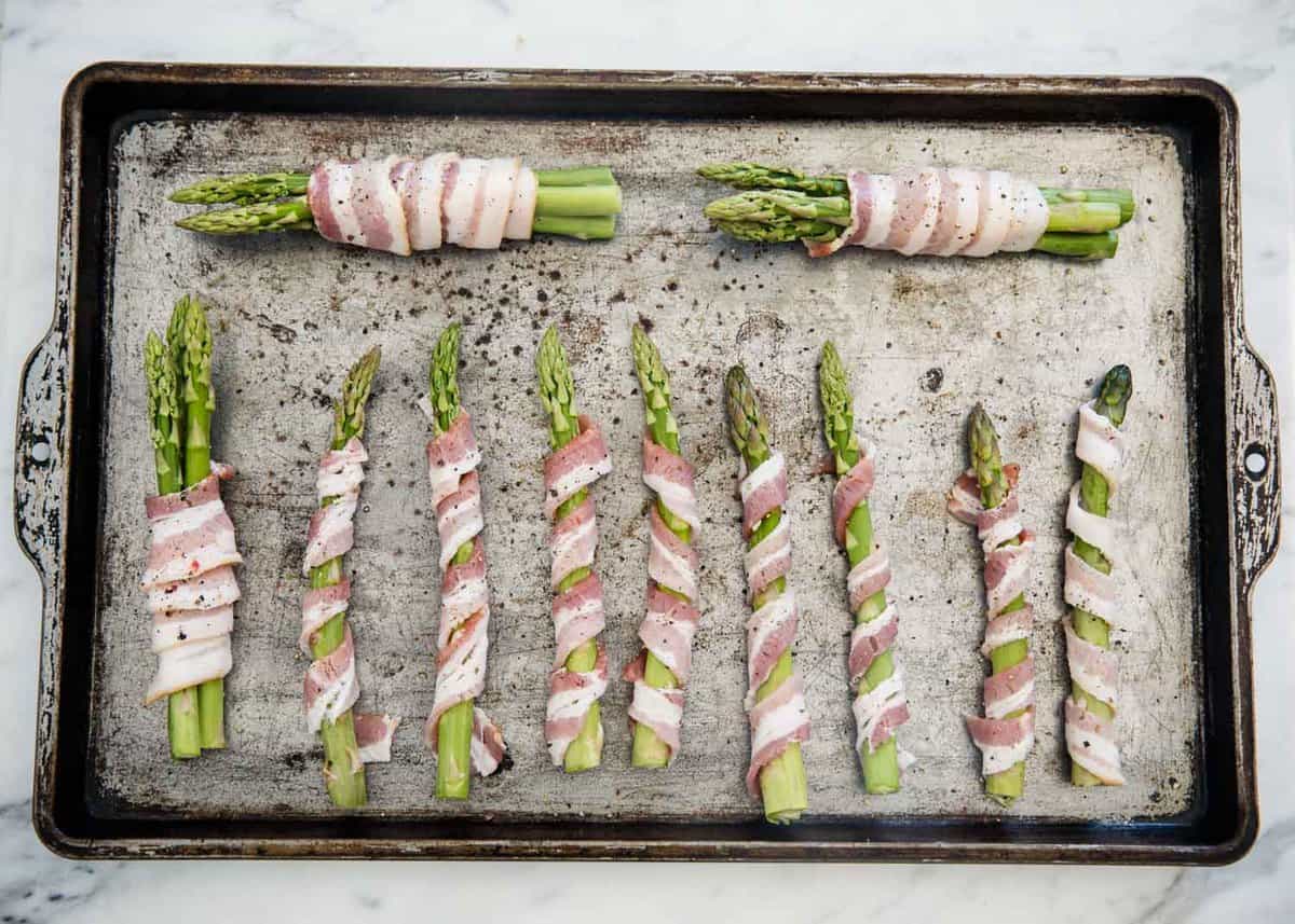 Bacon wrapped asparagus on baking sheet.