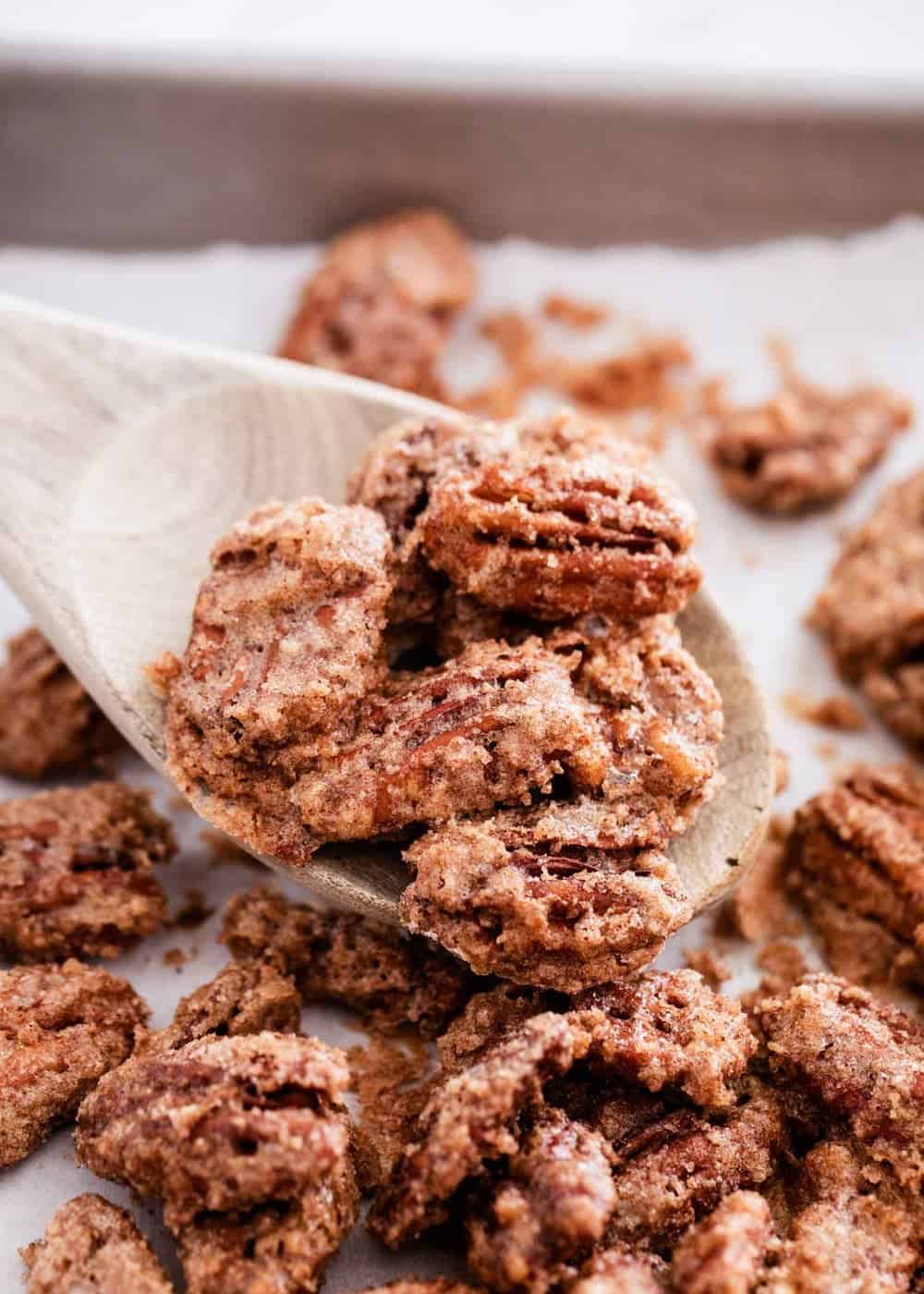 Candied pecans on baking sheet with wooden spoon.