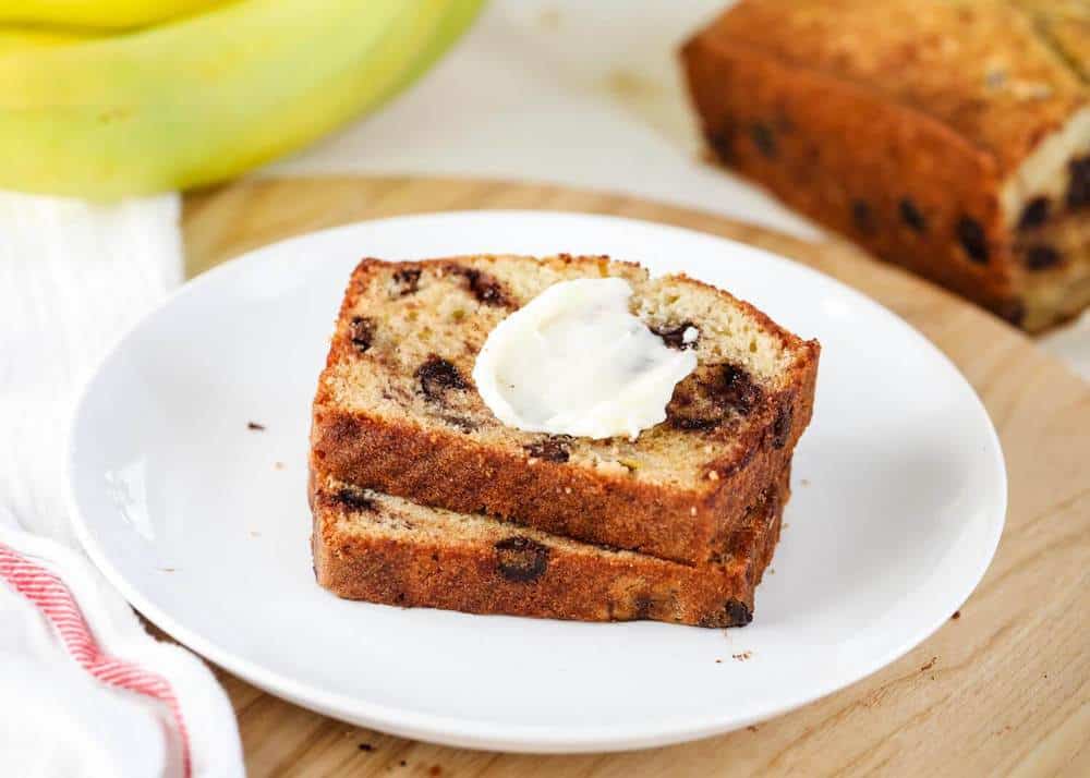 The BEST chocolate chip banana bread that's super soft, sweet and absolutely delicious! Filled with chocolate chips and fresh banana flavor. This recipe is always requested by friends and family! two pieces of chocolate chip banana bread with butter on top