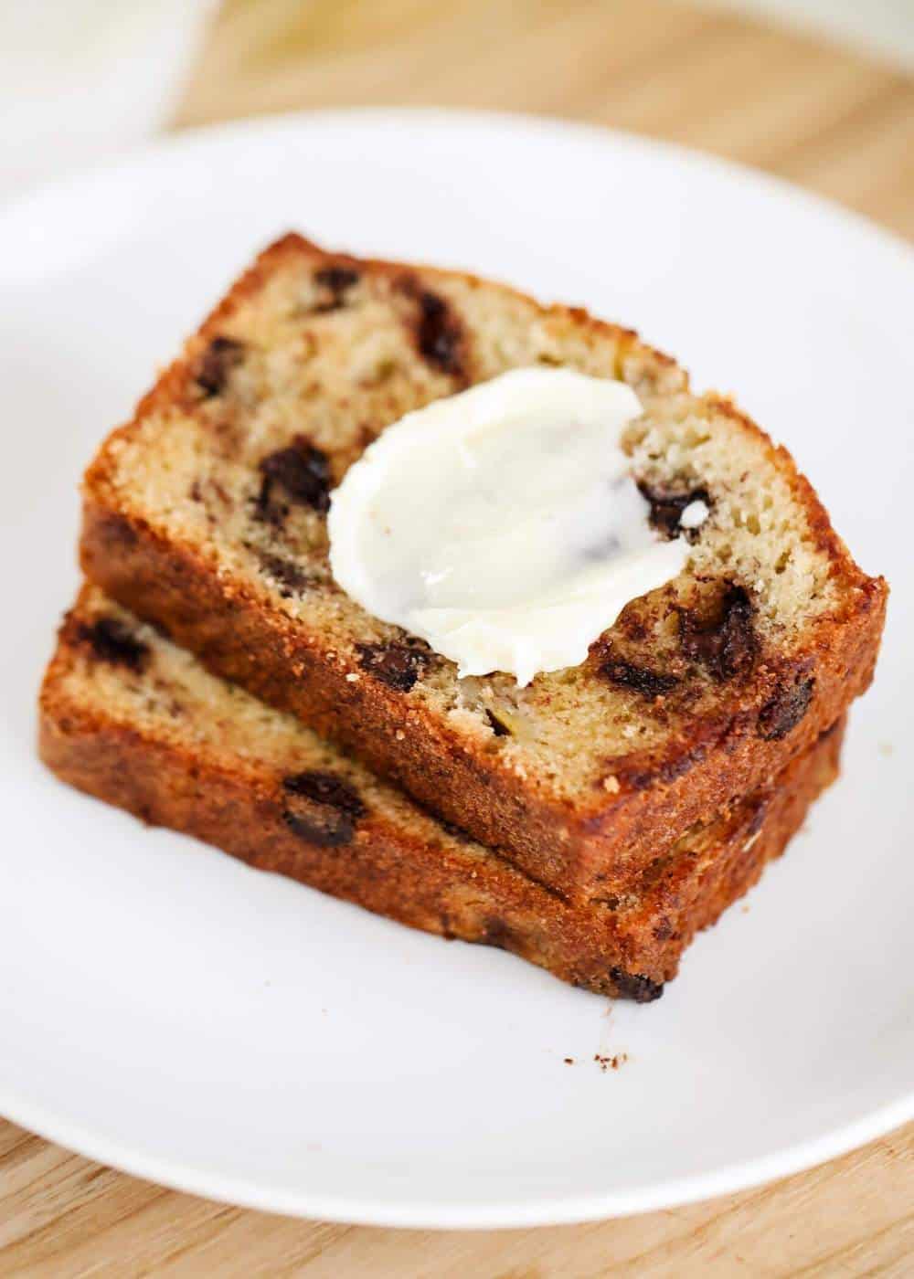 Chocolate chip banana bread on a white plate with butter on top.