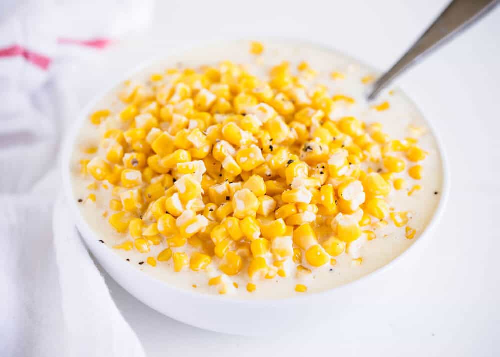 Creamed corn in a white bowl with a spoon.