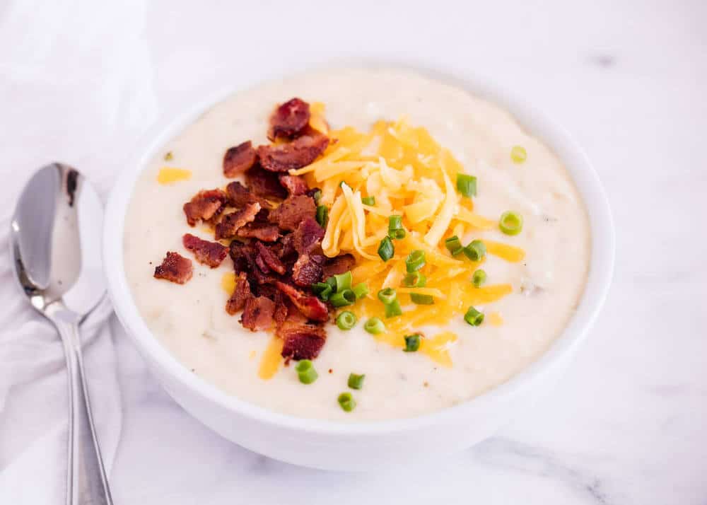 bowl of crockpot potato soup topped with bacon, cheese and green onions 