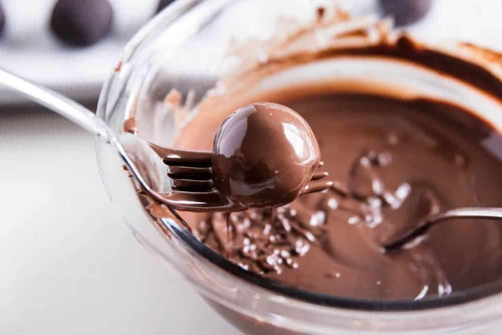 Dipping cookie dough truffles in chocolate with a fork.