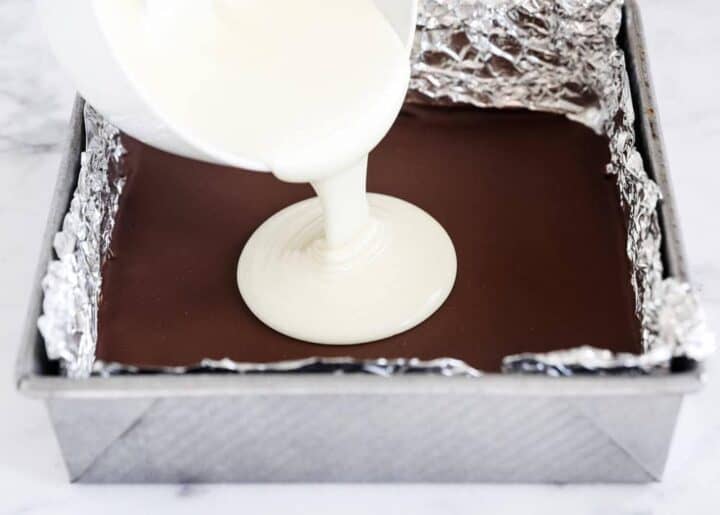 pouring melted white chocolate over dark chocolate in pan 
