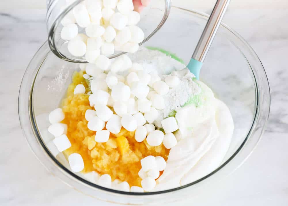 Pouring mini marshmallows into a glass bowl.