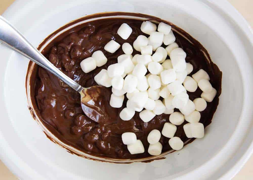 Mixing marshmallows into rocky road candy in crockpot.