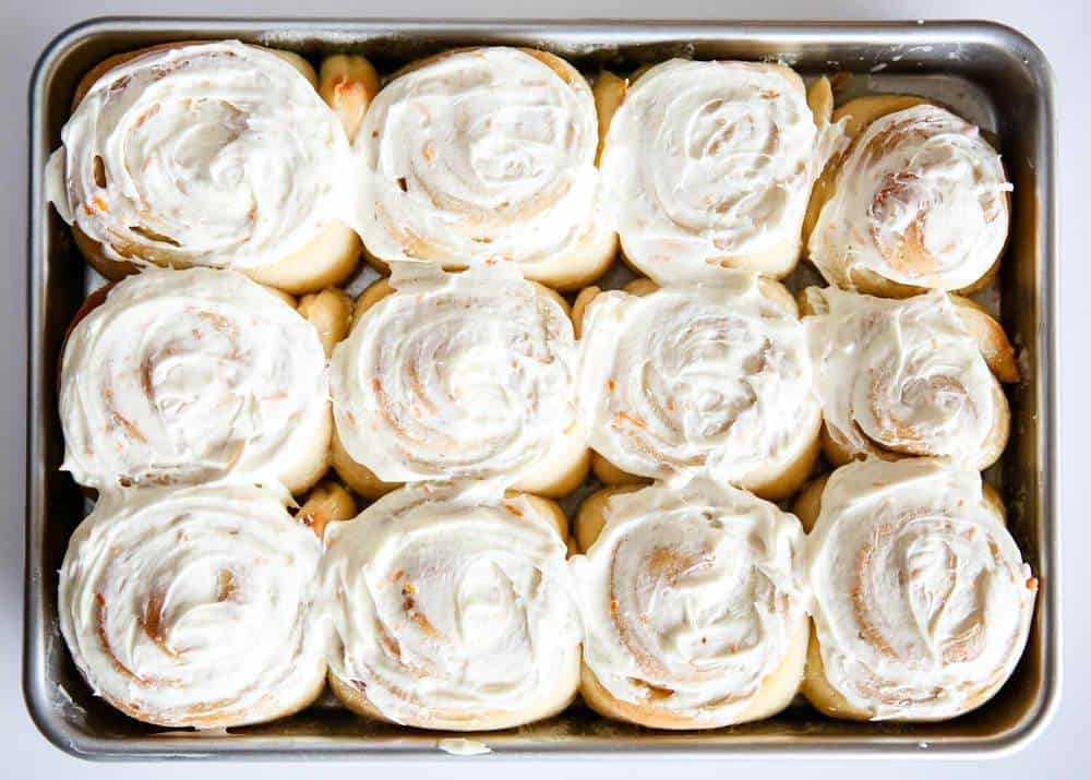 Orange sweet rolls in pan with frosting.