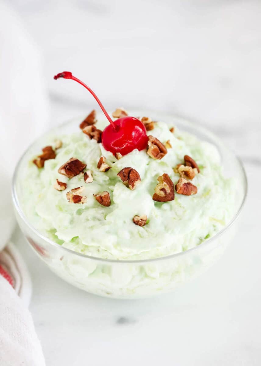 pistachio pudding salad in a glass bowl with a cherry on top 