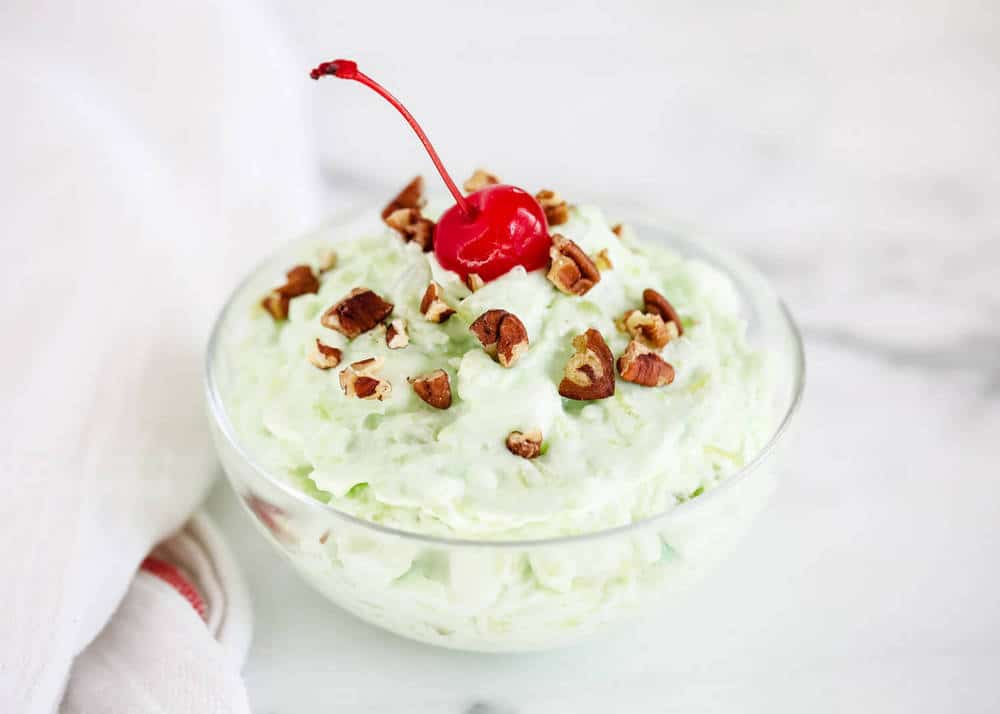Watergate salad in a glass bowl with a cherry on top.