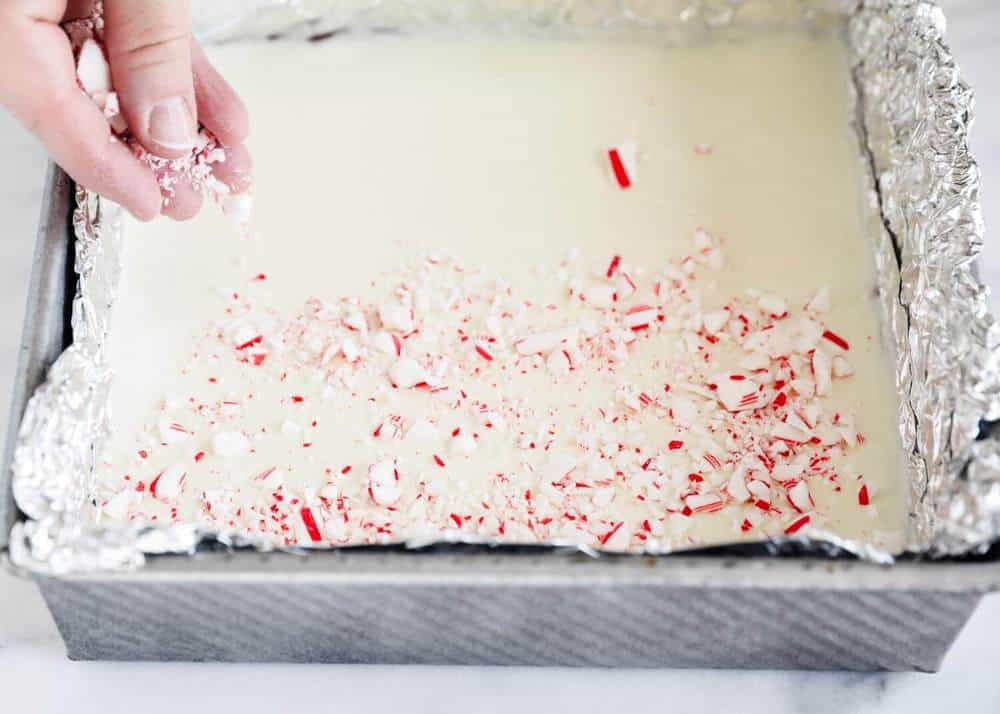 Adding crushed peppermint on top of peppermint bark.