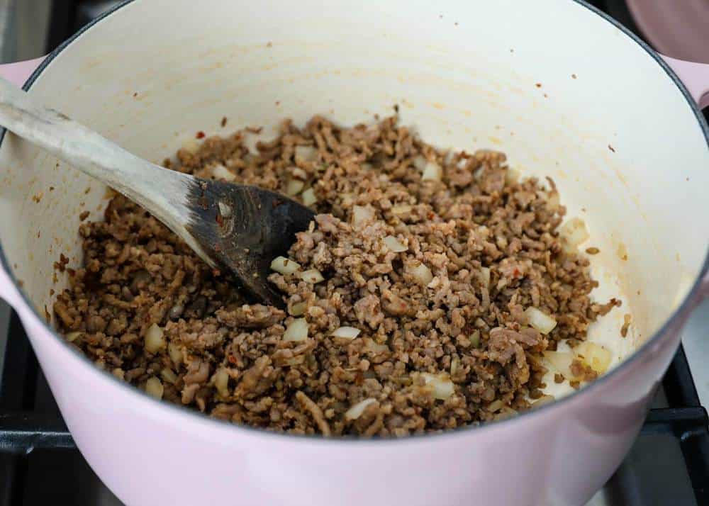 Cooking sausage and onions in pan with wooden spoon.