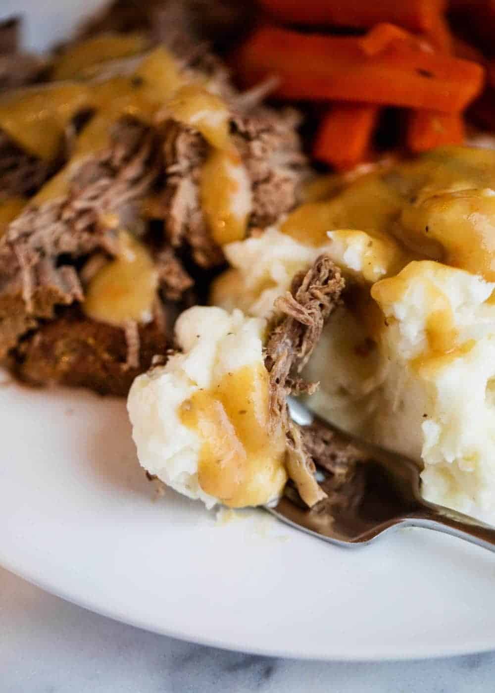 Pot roast on plate with mashed potatoes and gravy.