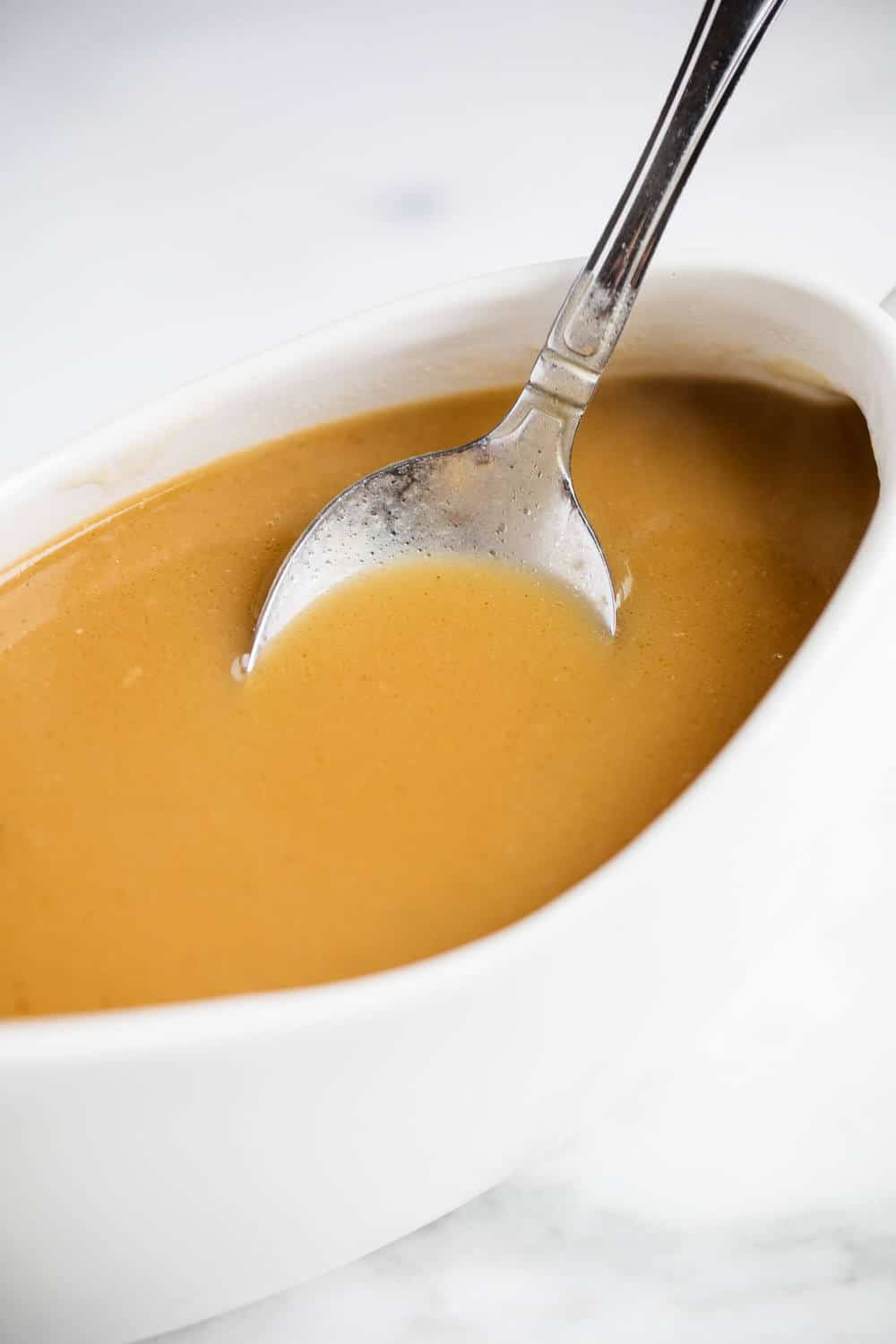 Brown gravy in a white gravy boat with a spoon.