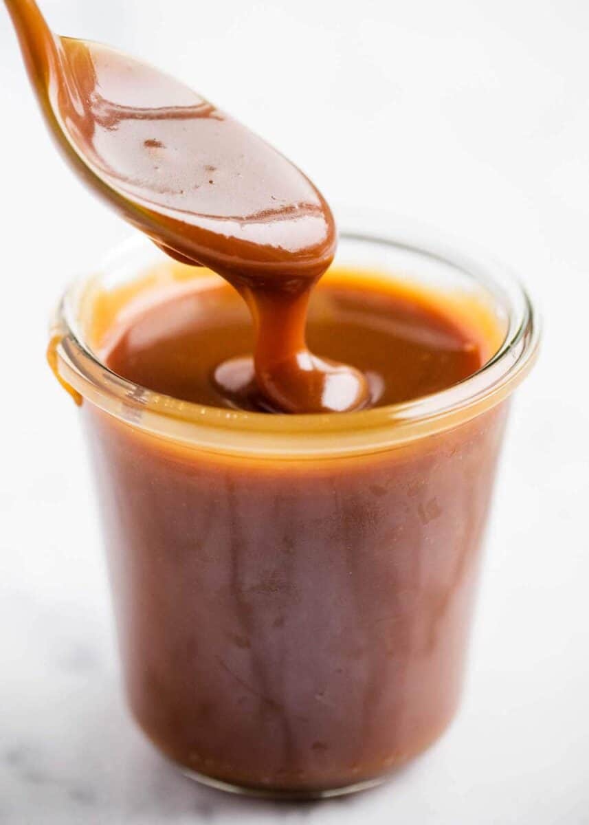 dripping spoonful of caramel sauce into glass jar 