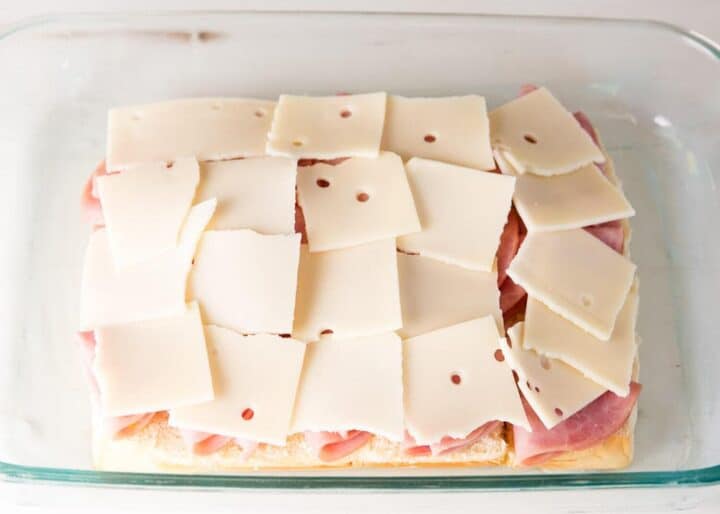 Hawaiian rolls with ham and cheese slices in baking dish 