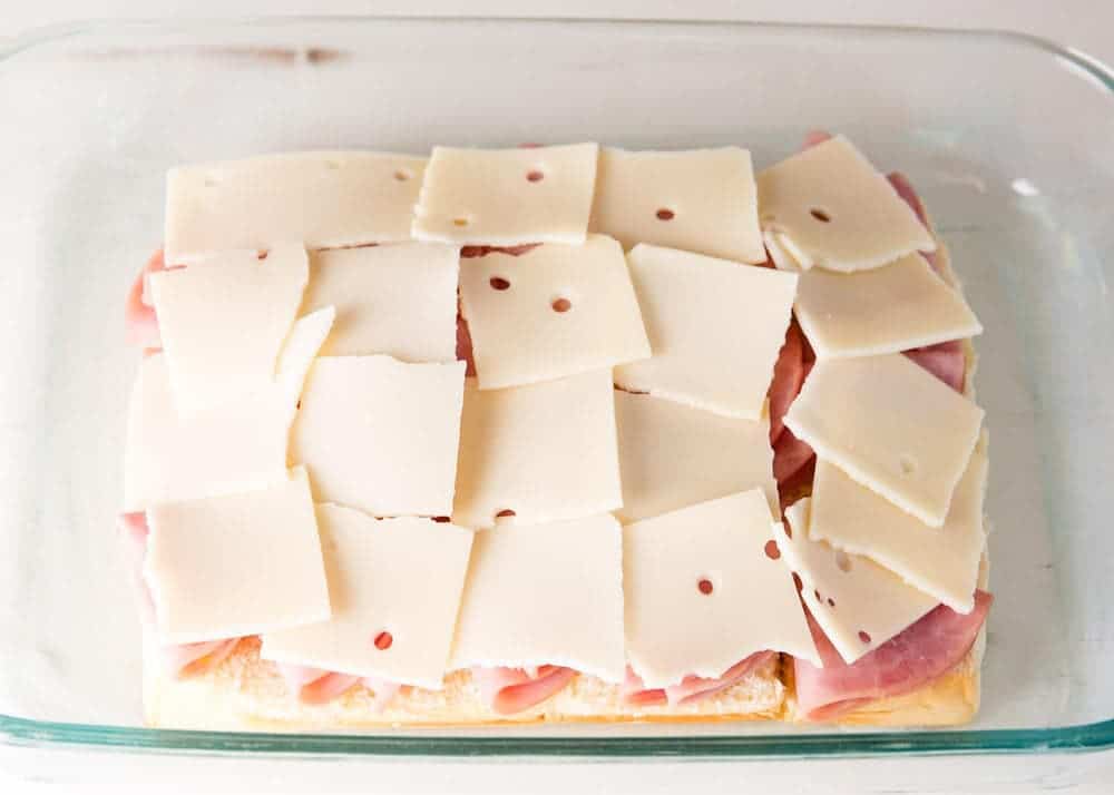 Hawaiian rolls with ham and cheese slices in a baking dish. 