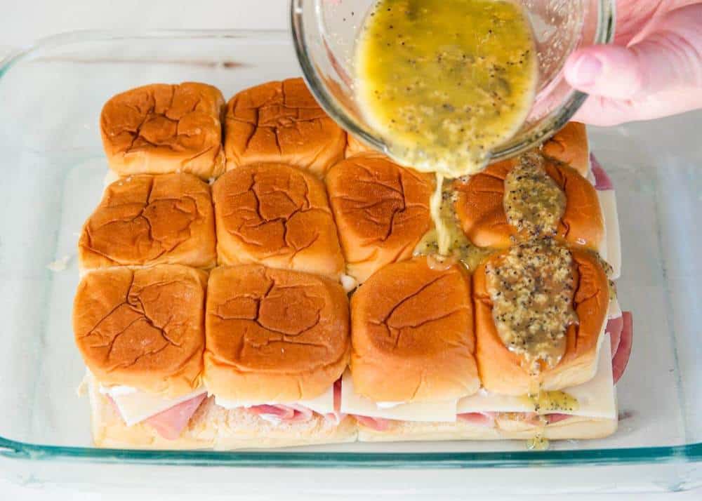 Pouring poppy seed sauce over ham and cheese rolls.