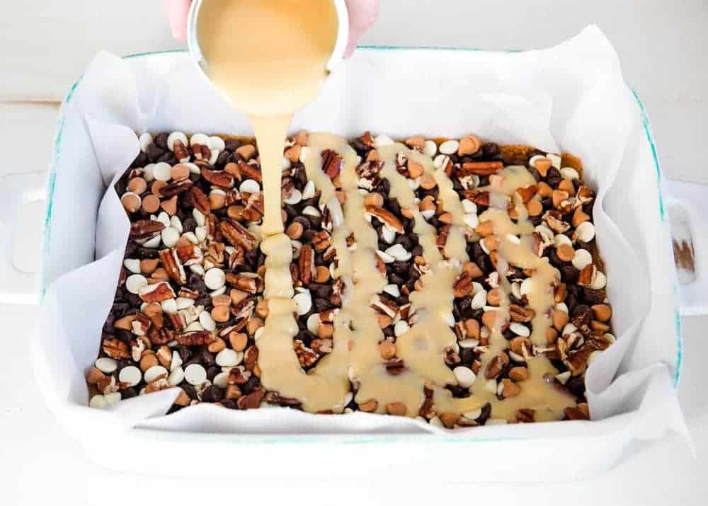 Pouring condensed milk on top of seven layer bars.
