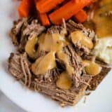 pot roast on a plate with gravy, mashed potatoes and carrots