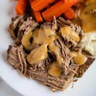 pot roast on a plate with gravy, mashed potatoes and carrots