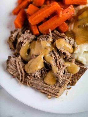 pot roast on a plate with gravy, mashed potatoes and carrots