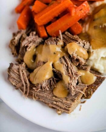 pot roast on a plate with gravy, mashed potatoes and carrots