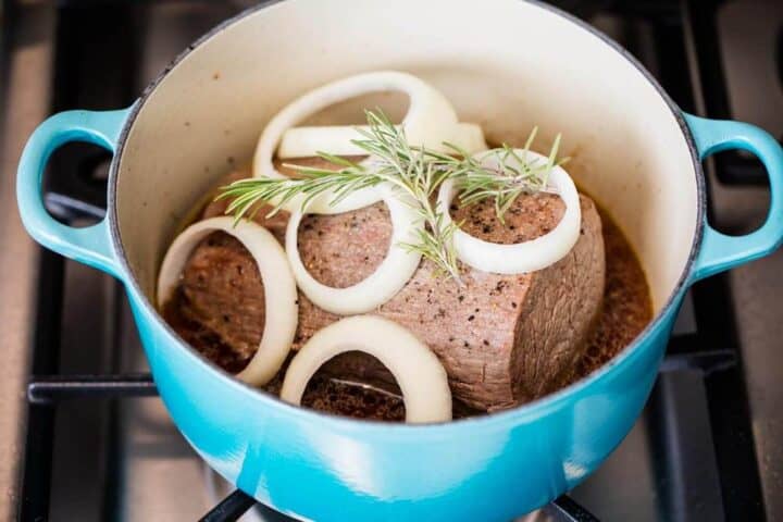 pot roast in pan with fresh onions and rosemary 