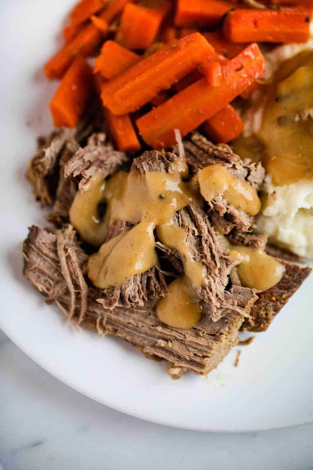 Pot roast on a plate with gravy, mashed potatoes and carrots.