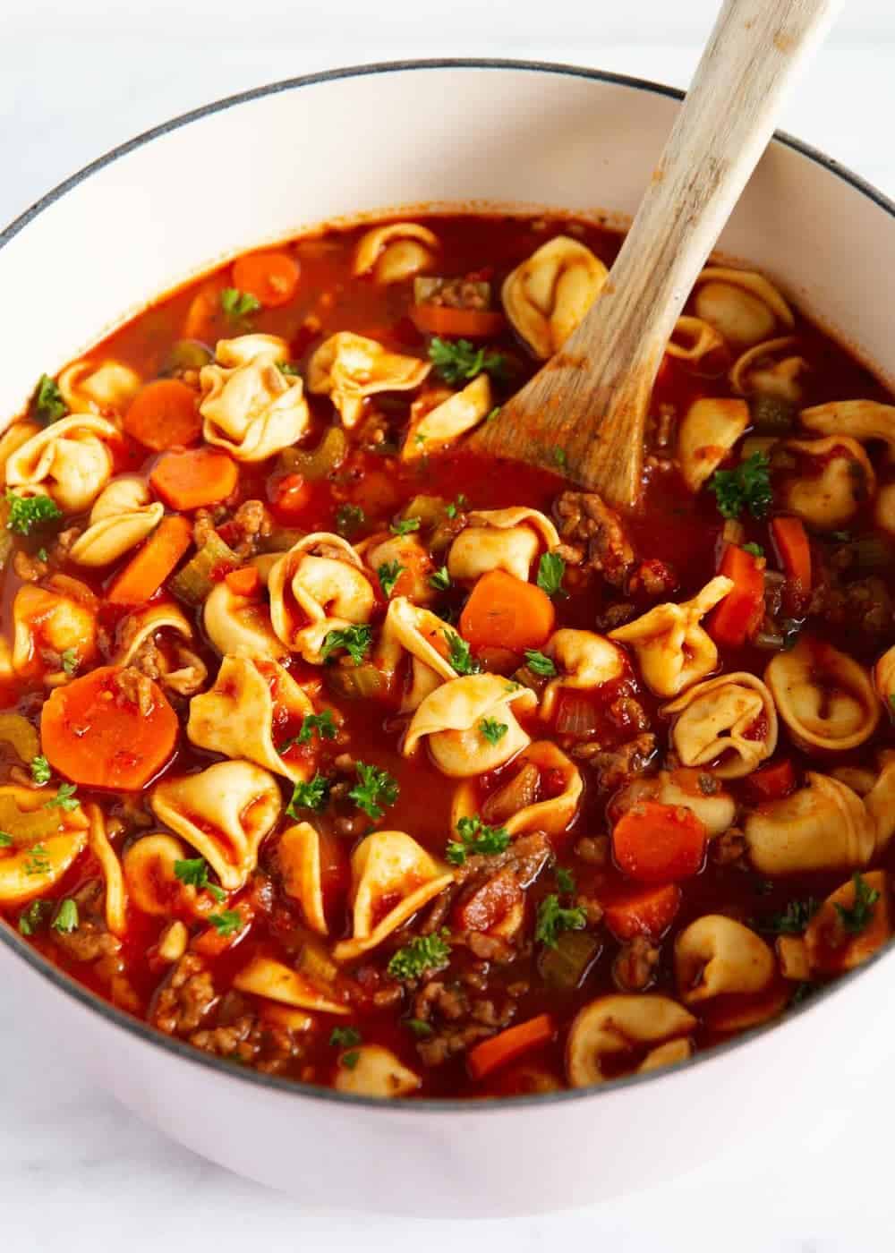 Sausage and tortellini soup in pot with wooden spoon.