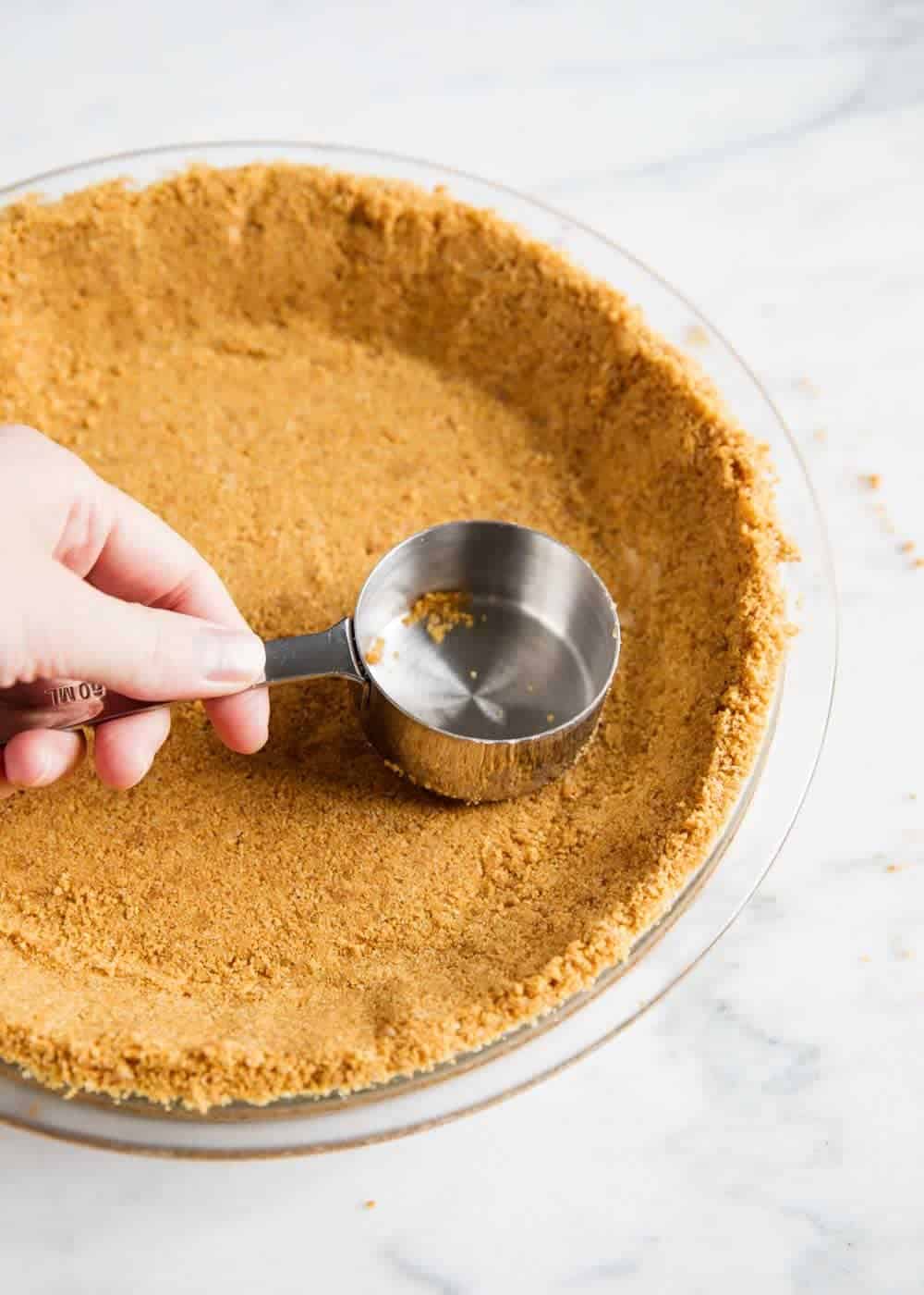 Bottom of measuring cup pressing into graham cracker pie crust.