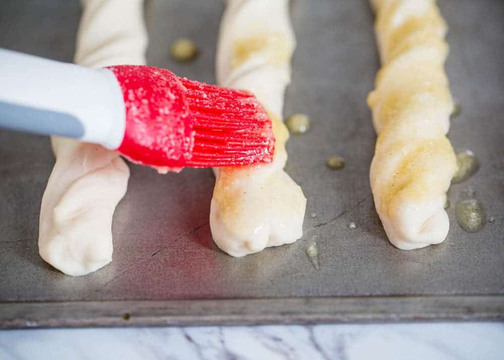Brushing parmesan butter topping on top of breadsticks.