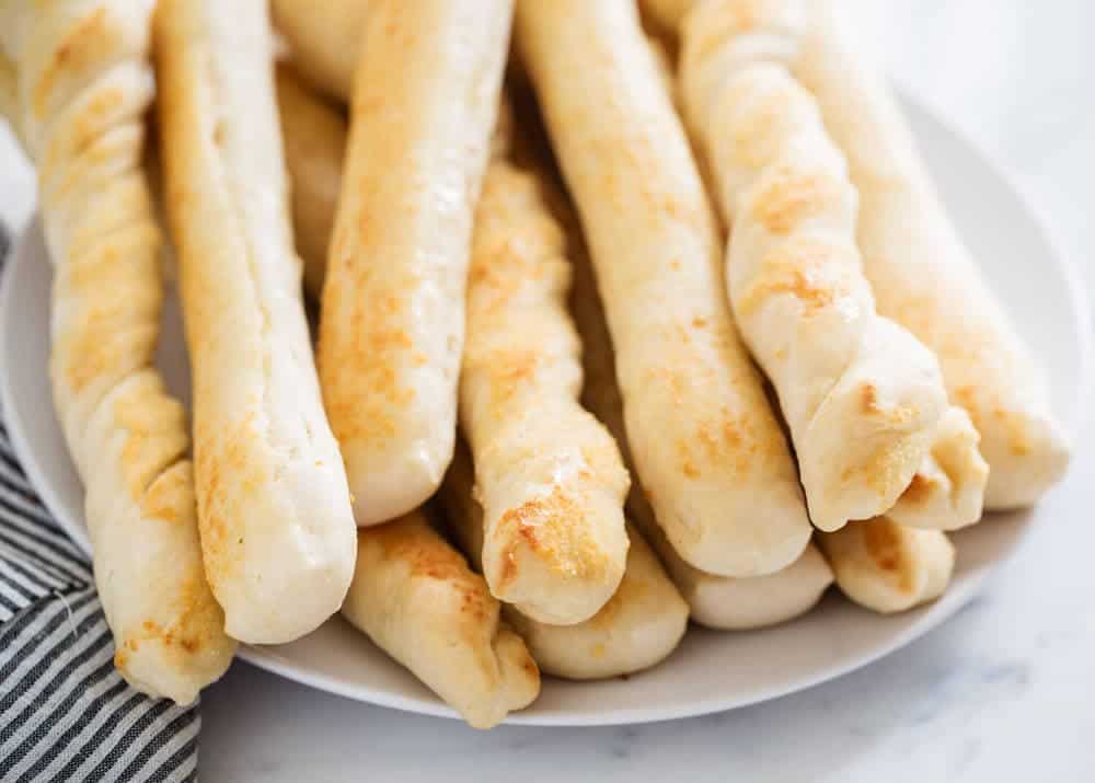 Stack of breadsticks on a white plate.