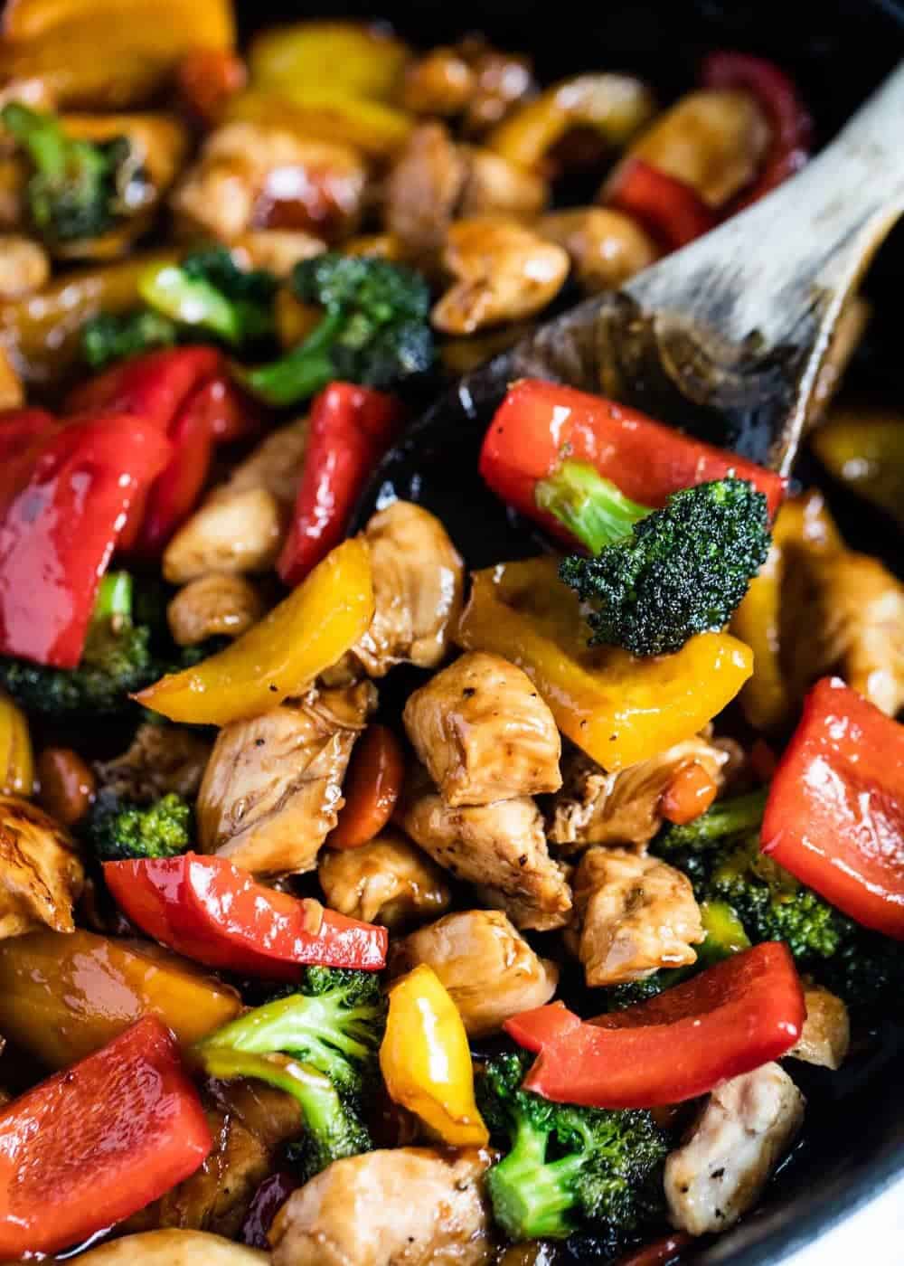 Close up of chicken and vegetable stir fry with wooden spoon.