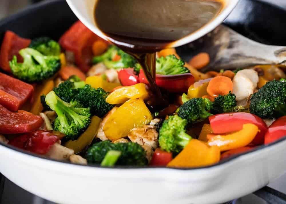 Pouring stir fry sauce over chicken and vegetables in pan.