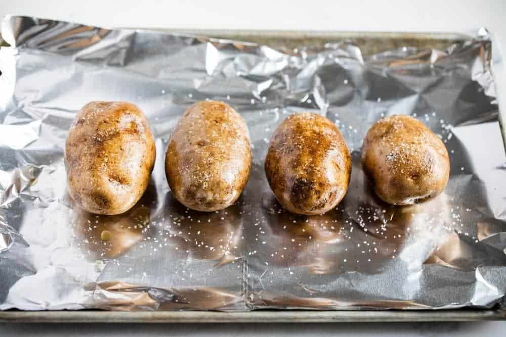 Baked potatoes on a baking sheet lined with foil.