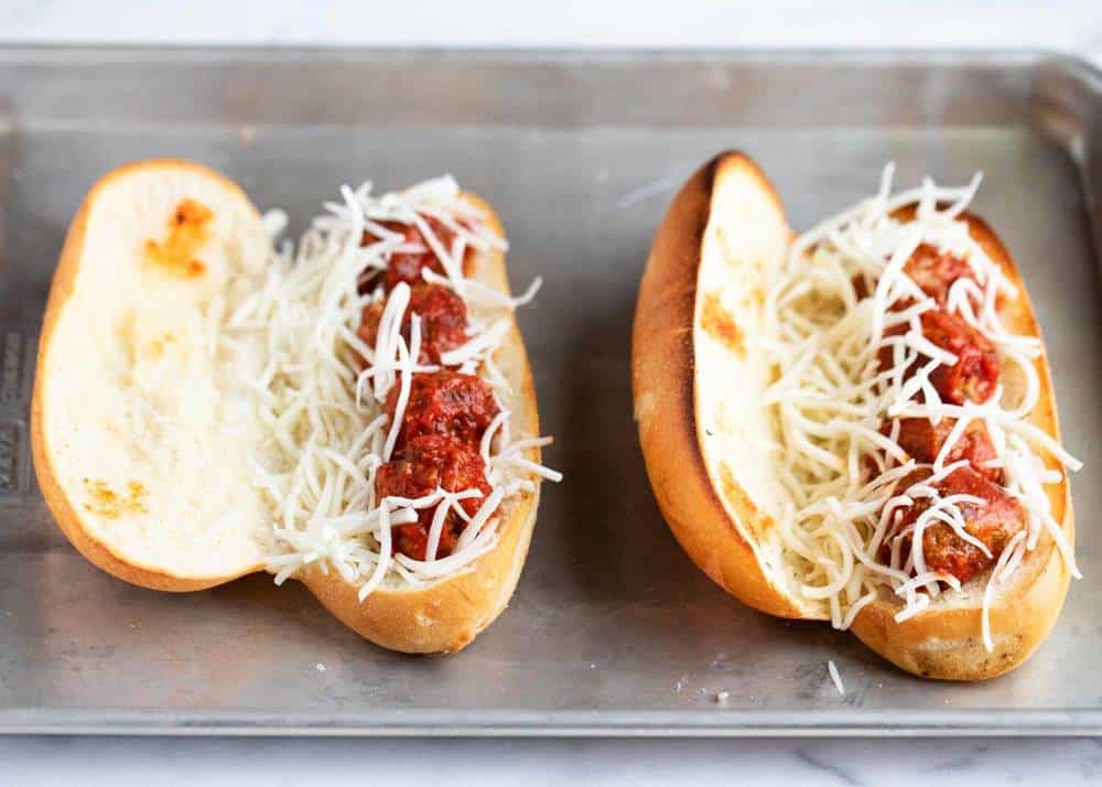 Assembling meatball subs on a baking sheet.