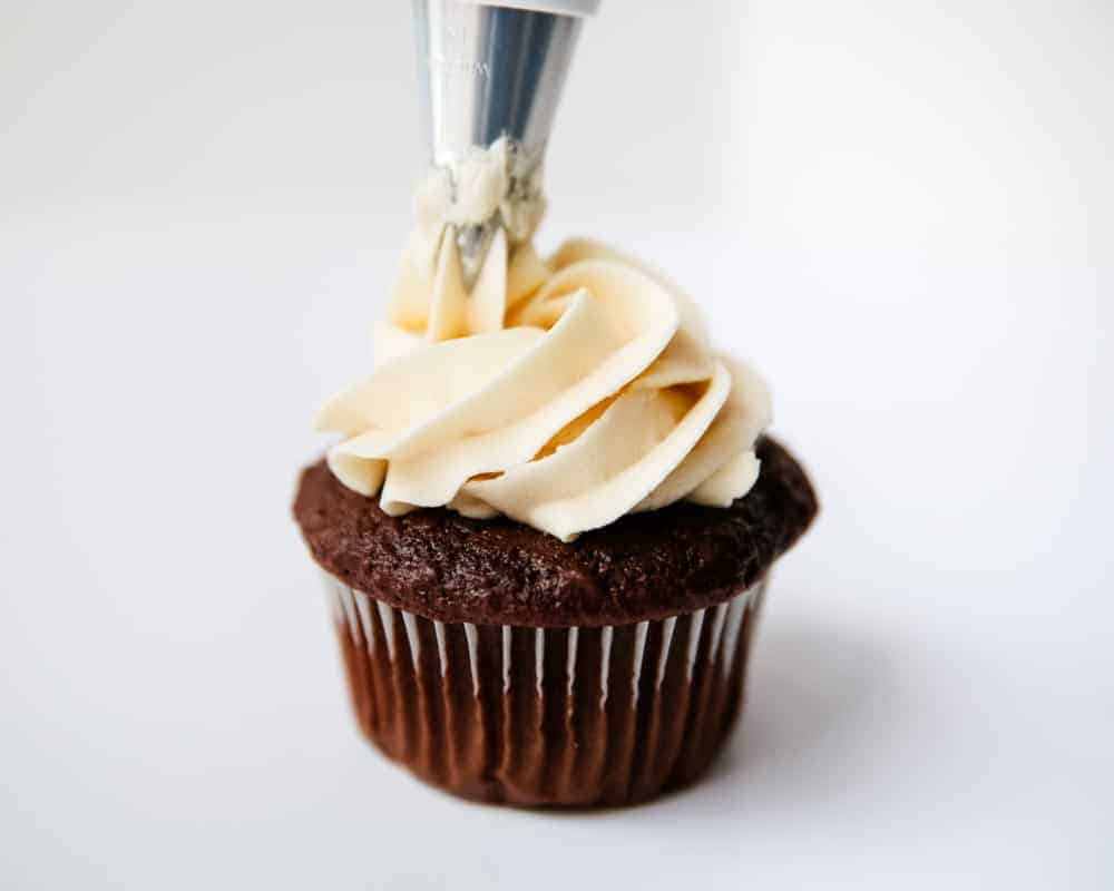 Piping buttercream frosting on top of chocolate cupcake.
