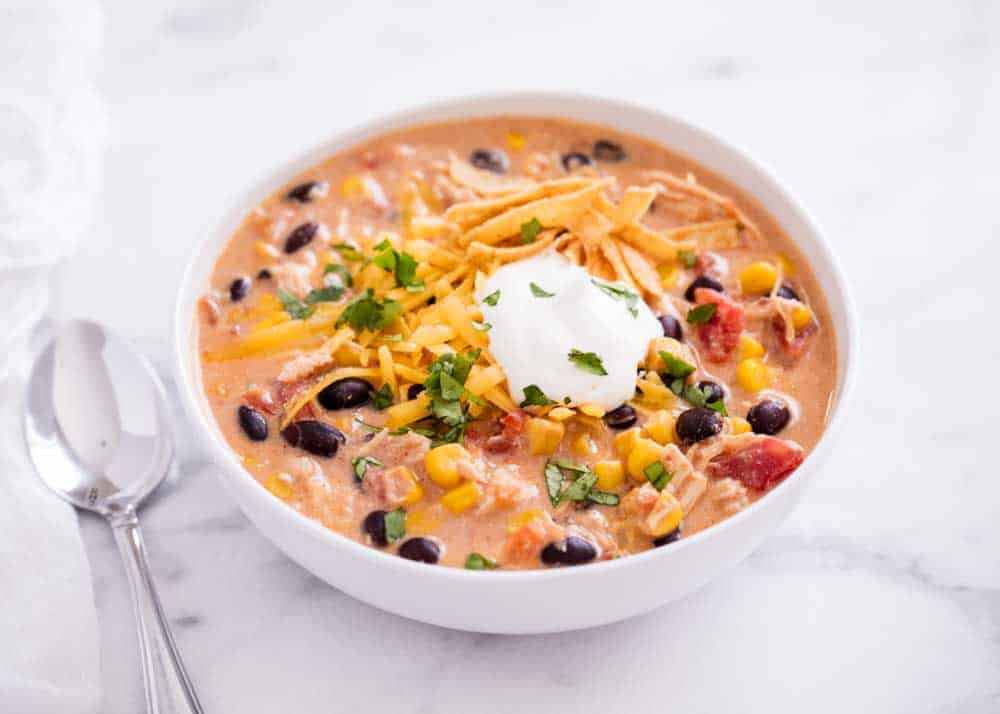 Chicken enchilada soup in a white bowl with tortilla strips, cheese and sour cream.