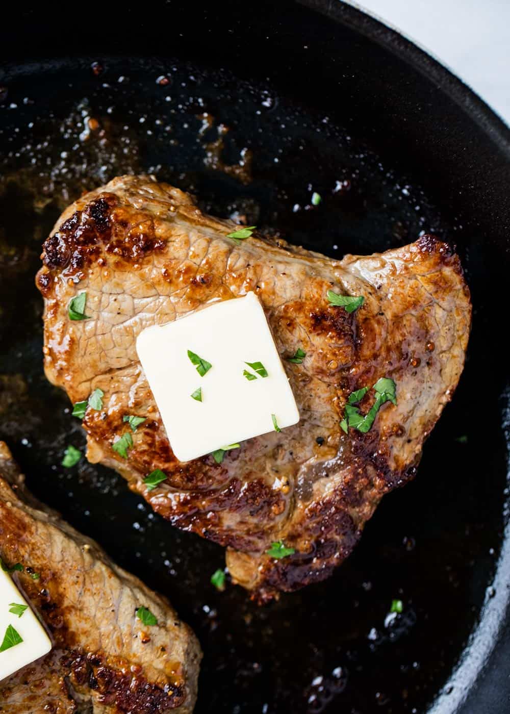 Closeup or steak in skillet with butter on top.