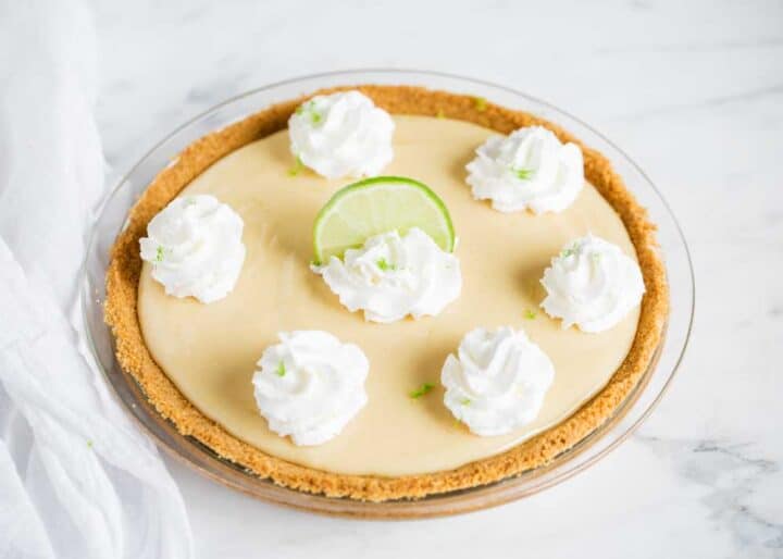 key lime pie topped with dollops of whipped cream and a lime slice
