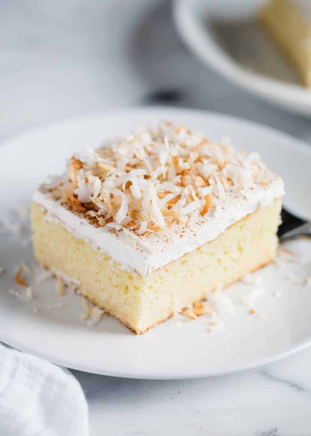 Slice of tres leches cake with toasted coconut on top.