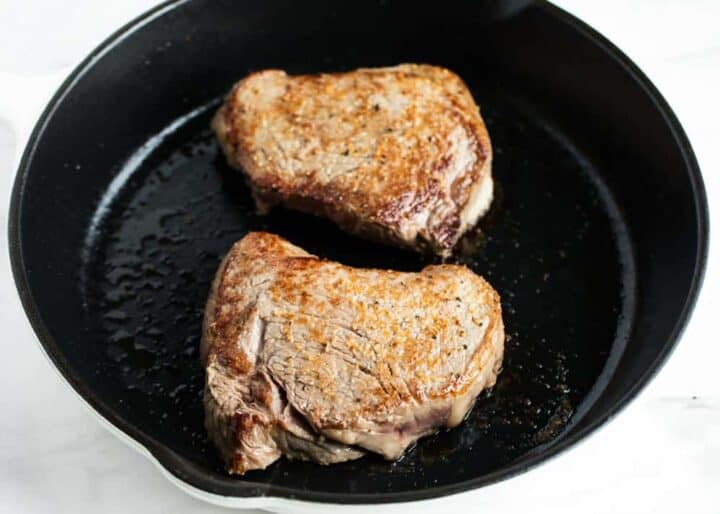 Learn how to cook steak in the oven in just 20 minutes! Use these simple tips and tricks to create the perfect steak that's caramelized, juicy and tender. You'll never cook steak any other way! 2 steaks in a cast iron skillet