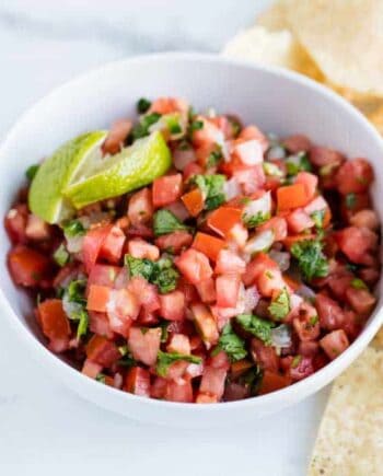 A bowl of quick and easy pico de gallo with tortilla chips to the side for scooping the fresh dip.