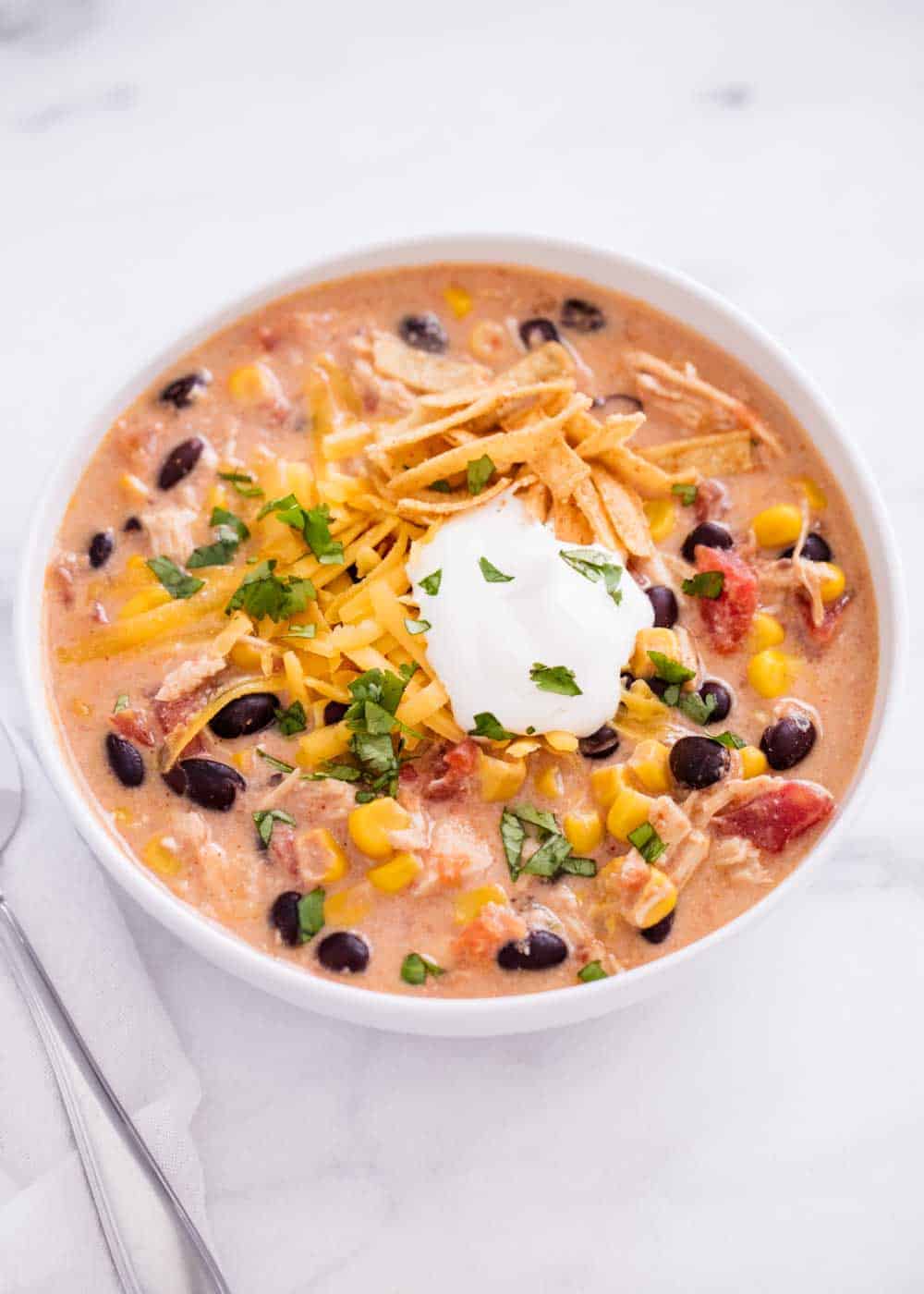 bowl of slow cooker chicken enchilada soup with tortilla strips, sour cream, cheese and cilantro