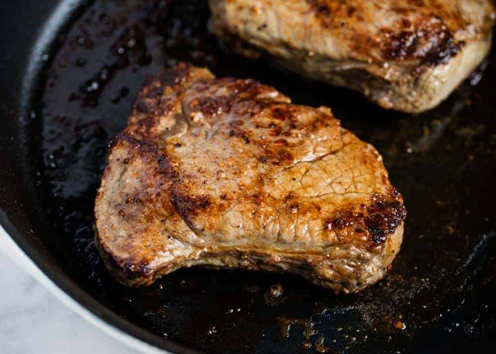 Charred steak in a black skillet.