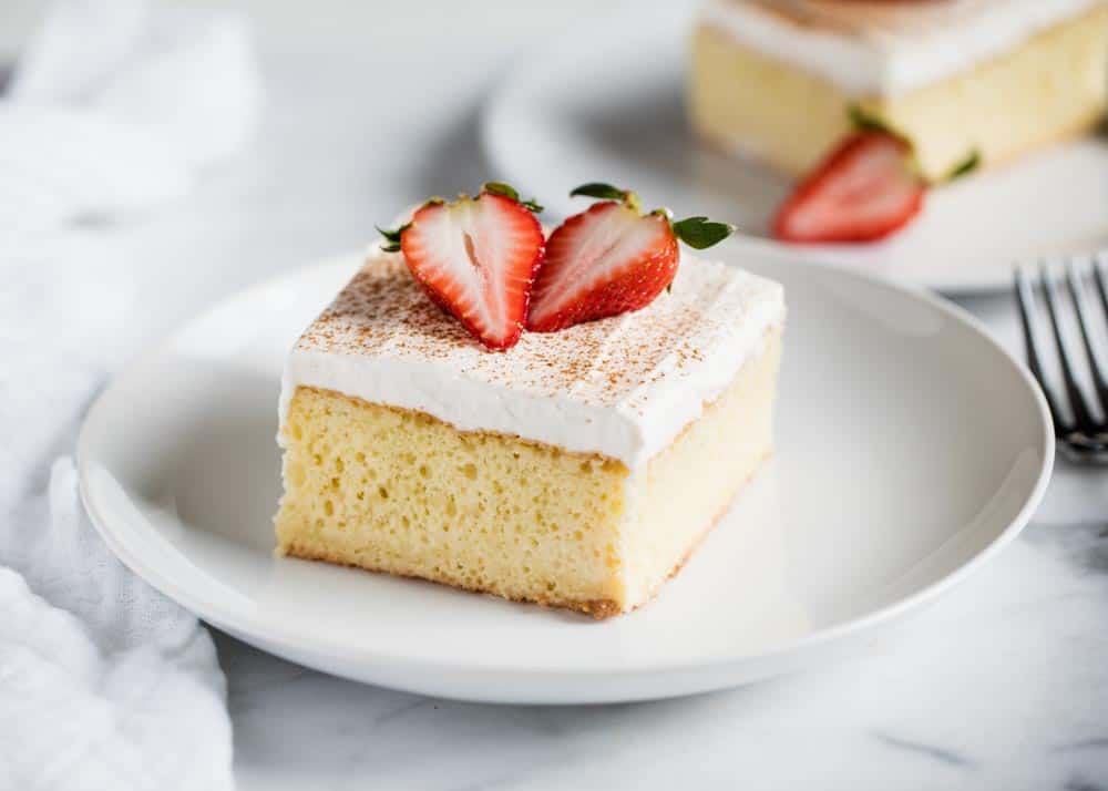 Slice of tres leches cake on a white plate.
