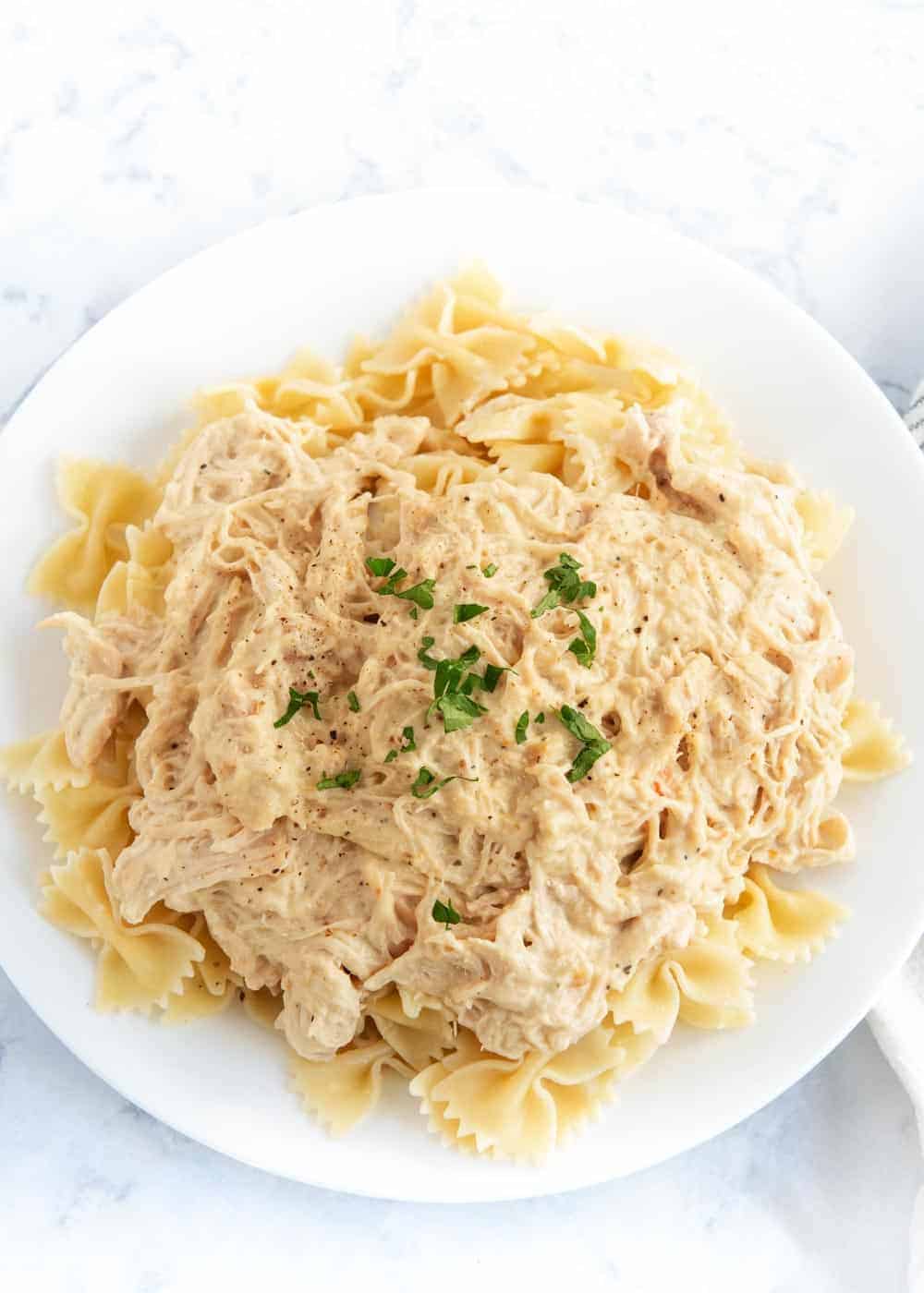 Creamy Italian chicken served over noodles on a white plate.