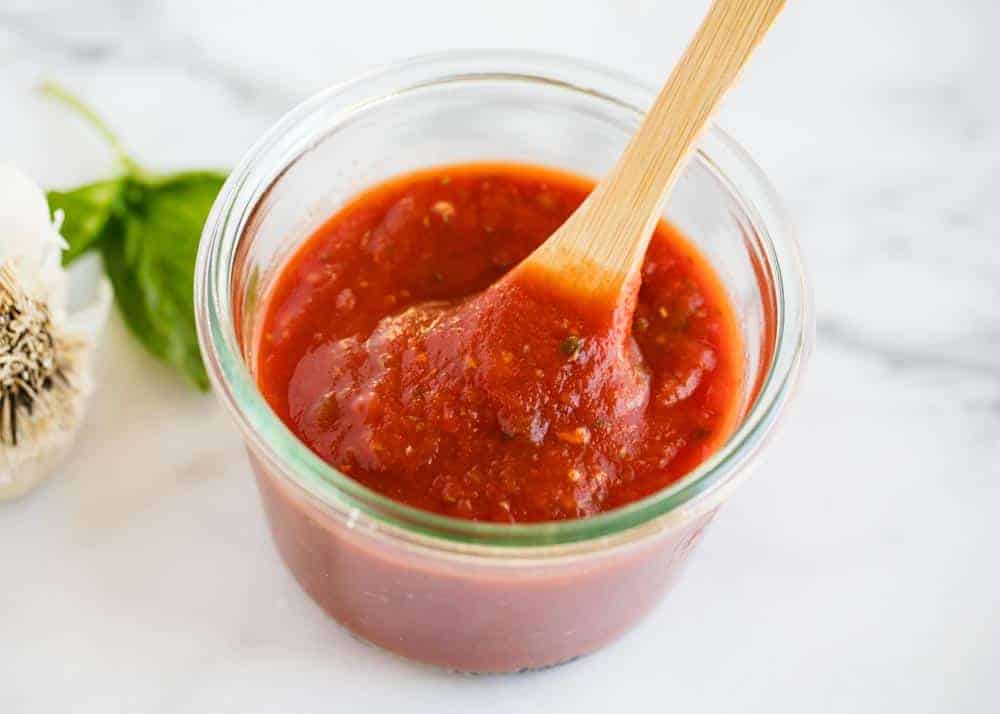Pizza sauce in jar with wooden spoon.