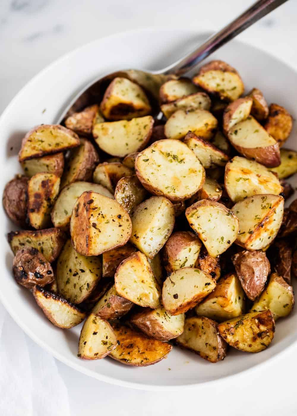 Roasted red potatoes in bowl with spoon.
