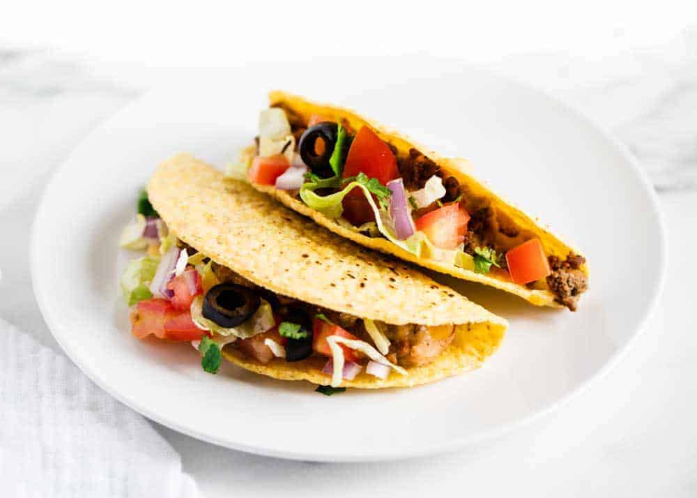 Two ground beef tacos on white plate.